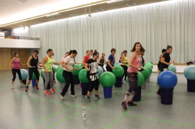 Frauen beim Aerobic-Training: mit Trommelstöcken auf Gymnastikbällen in der Halle